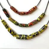 Three beaded necklaces with tubular glass segments in brown, olive, and yellow tones arranged horizontally.