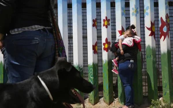 Community mural installation with children and adults interacting, featuring painted designs with red and green tones on a white fence or wall.