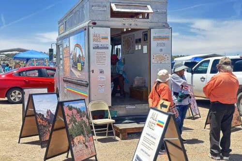 Mobile gallery or art exhibition vehicle parked in outdoor lot with visitors and signage, displaying artwork and educational materials.
