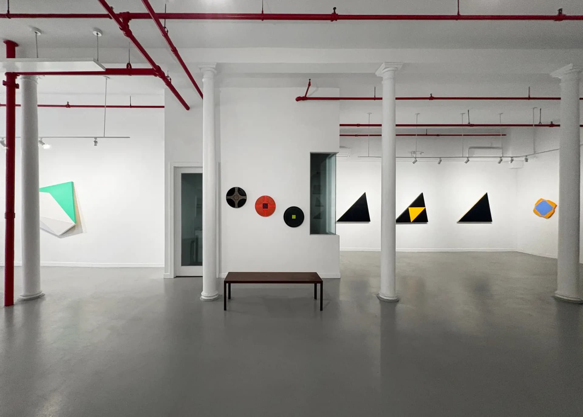 Gallery interior with polished concrete floor, white walls, and red overhead ductwork displaying colorful geometric paper installations.
