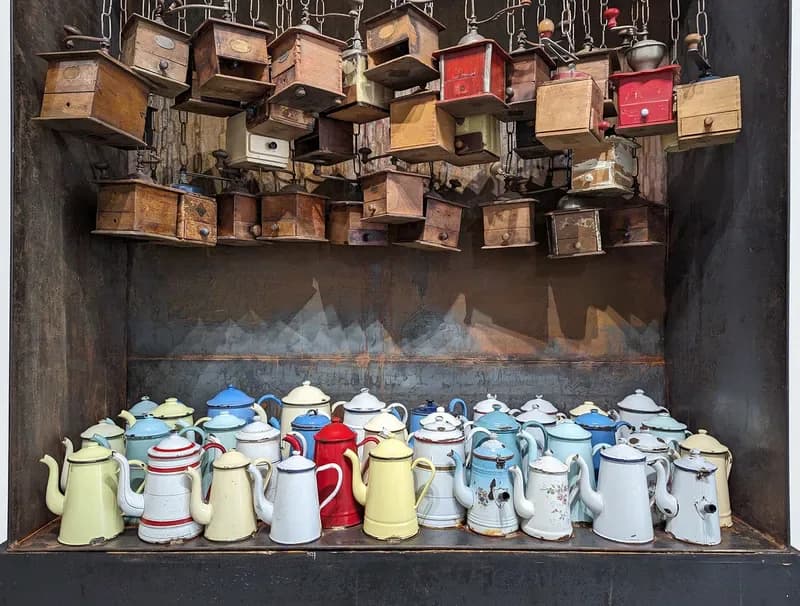 Mixed-media installation with suspended wooden boxes above a collection of vintage ceramic teapots and vessels arranged on a shelf.