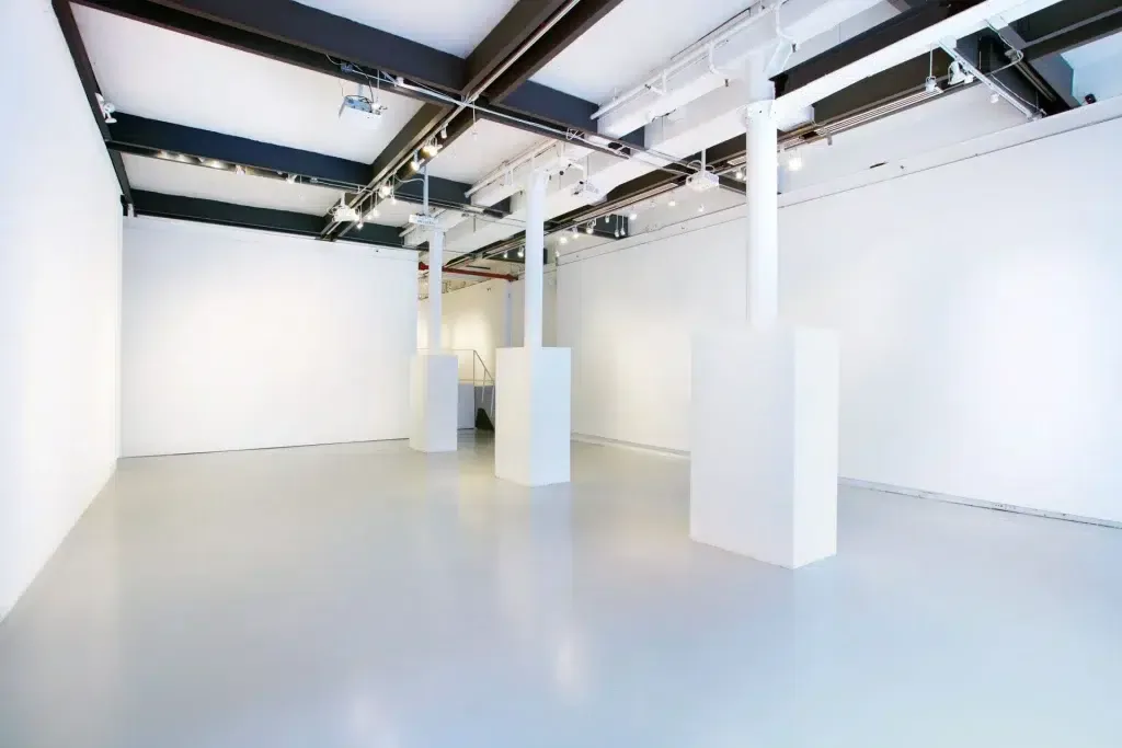 White Space Chelsea's minimalist gallery interior with polished concrete floor, white walls, exposed black ceiling beams, and white support columns.