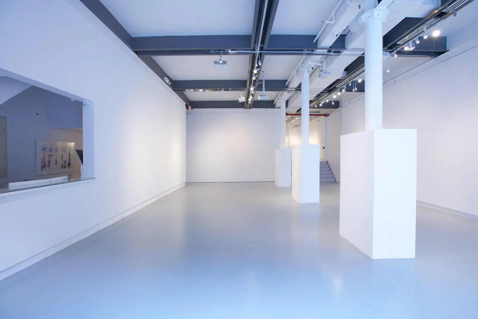 Gallery interior with white walls, polished floor, industrial ceiling with dark beams, white columns, and track lighting in White Space Chelsea.