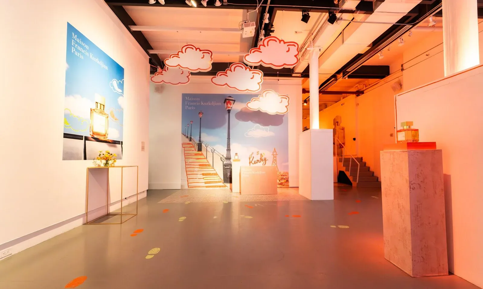 White Space Chelsea gallery with warm orange ambient lighting, white pedestals, mounted artwork, and polished floor reflecting warm tones.