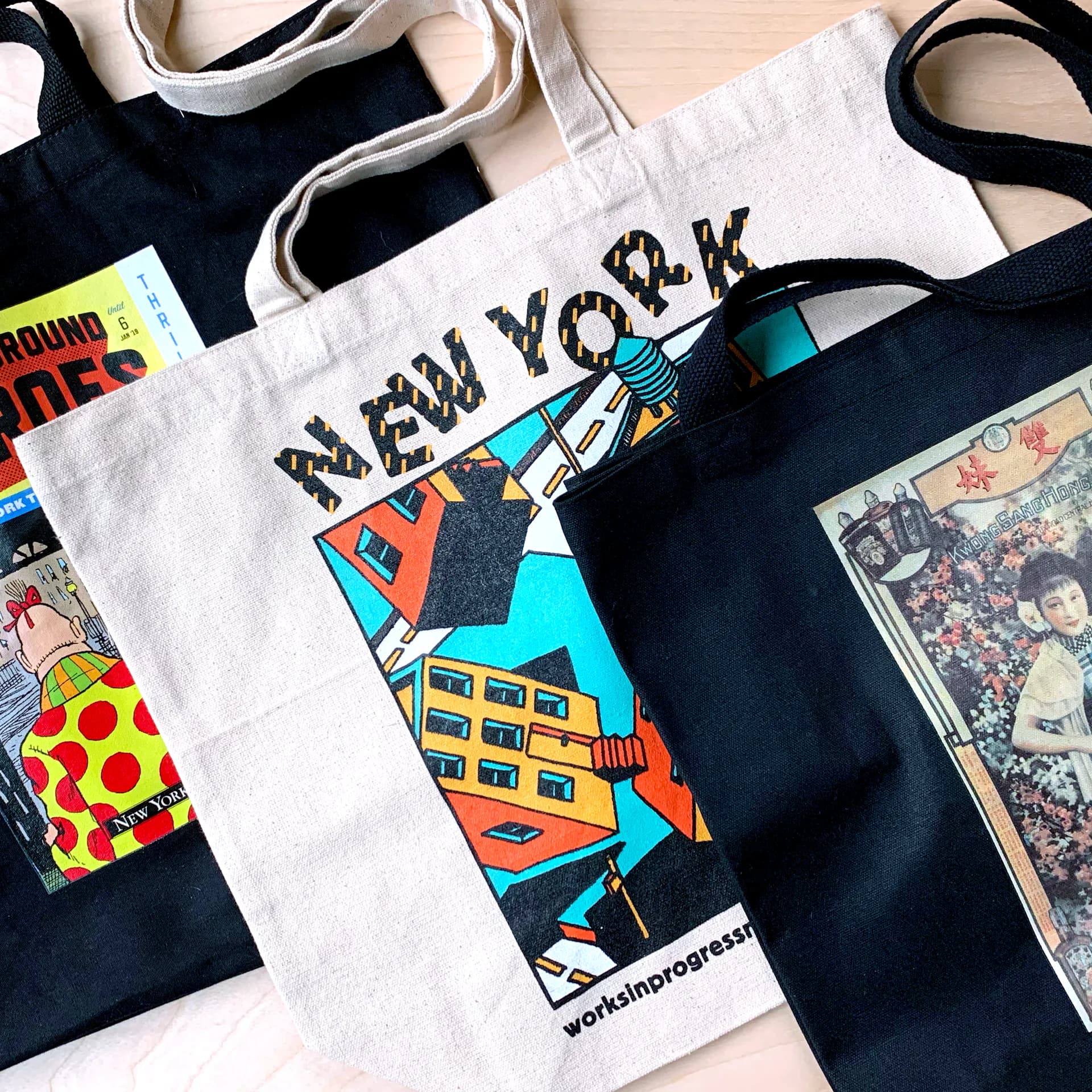 Tote bags and merchandise featuring New York-themed illustrations including cityscapes, pizza, and colorful graphic designs in bold colors.