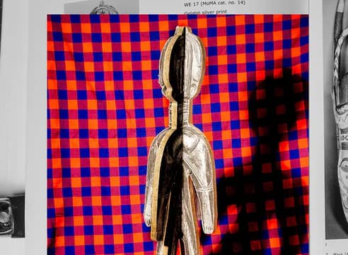 Pale wooden figure with elongated head against vivid red and blue checkerboard pattern background.