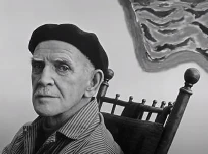 Black-and-white portrait of an older man wearing a beret and striped shirt, seated with artwork visible behind him.