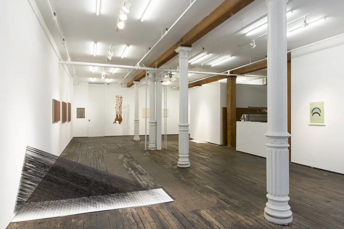 Gallery interior with white walls, wooden columns and beams, hardwood floor, and artworks displayed on the walls and floor